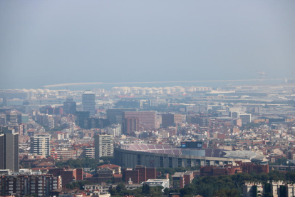 Barcelona amb el Camp Nou en primer pla i el port de fons amb boira per pol·lució al fons.