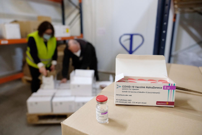 Vacunes en primer pla i operaris apilant caixes de vacunes d'AstraZeneca a Catalunya.