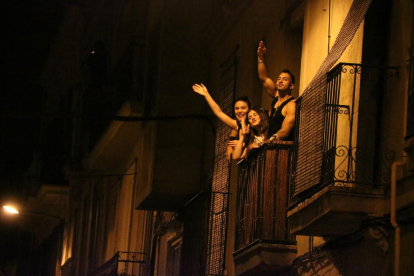 Tres jóvenes desde un balcón del barrio de Gracia celebran que acaba el toque de queda nocturno.