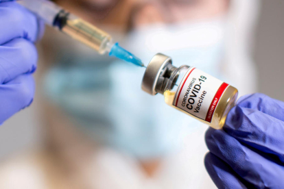 Una mujer tiene una jeringa médica y una botella pequeña con la etiqueta 'Vacuna contra el coronavirus COVID-19'