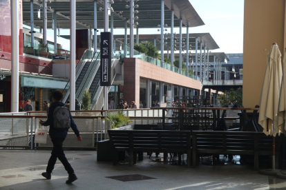 Un noi passejant pel costat de taules i cadires enretirades a un punt del centre comercial La Maquinista.