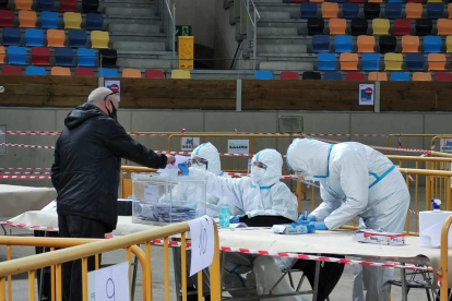 Una persona votando ante los miembros de una mesa electoral de la Tàrraco Arena Plaza que van equipados con EPI.