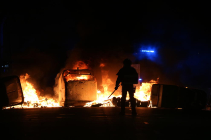 Silueta d'un agent dels antiavalots dels Mossos d'Esquadra davant de diversos contenidors cremats durant les protestes.