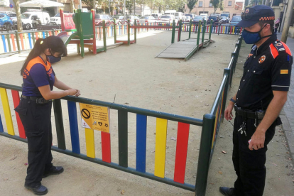 Dos voluntarios de Protección Civil de Salt poniendo una cinta en un parque infantil.