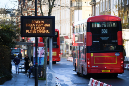 Un bus de Londres passa pel costat d'un cartell que alerta de l'alta incidència de la covid-19 a la capital britànica