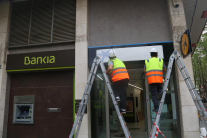 Una operarios cambiando los carteles de Bankia por los de CaixaBank en una oficina.