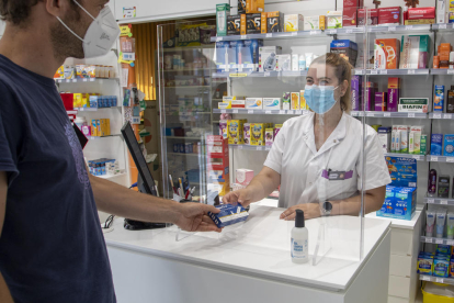 Una farmacéutica de la farmacia Salazar, en la calle Cuerpo del Bou, entrega una maceta de antígenos a un cliente.