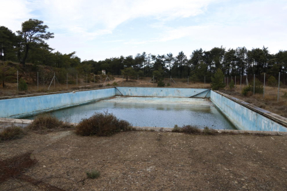 La piscina, mig buida d'aigua i degradada, de l'antic campament militar.