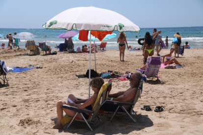 Plano medio de dos personas bajo un parasol en la playa de Salou.
