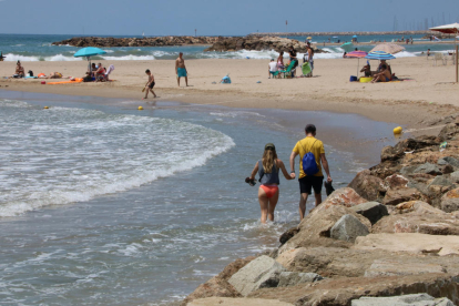 Una playa de Cunit sin arena, con dos bañistas cruzando con el agua en los tobillos.