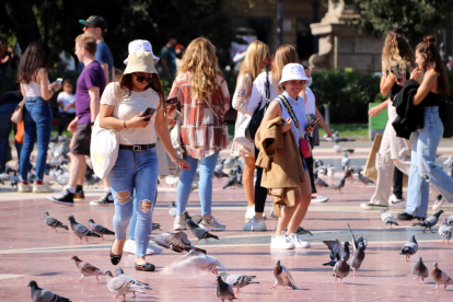 Unes turistes passegen entre coloms a la plaça de Catalunya de Barcelona.