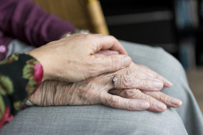 Primer plano de las manos cogidas de una cuidadora y una persona mayor con dependencia.