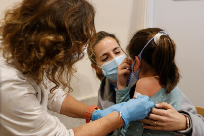 Una enfermera poniendo la tirita a una niña después de ponerle la vacuna.
