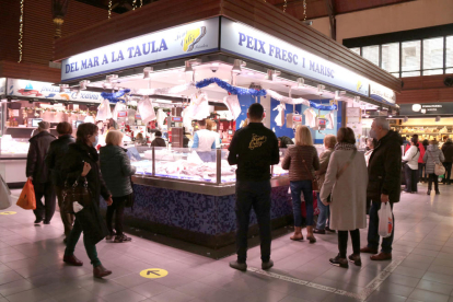 Compradores de espaldas comprando para|por Navidad en un puesto del Mercado Central de Tarragona.