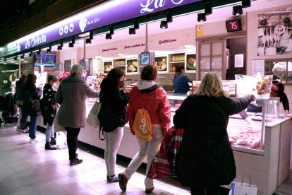 Compradores de espaldas comprando para|por Navidad en un puesto del Mercado Central de Tarragona.