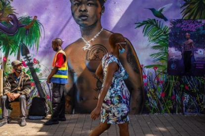 Una mujer con mascarilla por el coronavirus pasa junto a un grafiti en Johannesburgo, Sudáfrica.
