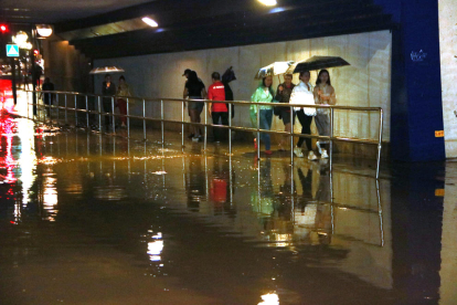 Un grup de persones passa per un pont del barri del Serrallo inundat per la pluja.