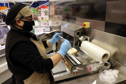 Una trabajadora envuelve un queso con un papel film compostable.