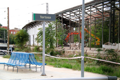 Un cartel de Tortosa de la estación de tren frente a las máquinas trabajando al fondo en el derribo de los antiguos almacenes.