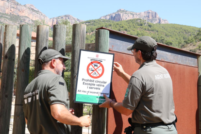 Dos Agents Rurals col·loquen un cartell informatiu a l'accés al Parc Natural de la Serra de Montsant.