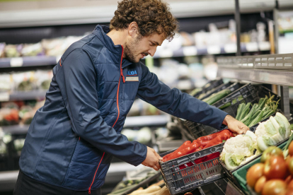 Un treballador d'un supermercat col·locant bé la secció de verdures.