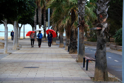 Tres mujeres pasean con paraguas por el paseo marítimo de Cambrils.