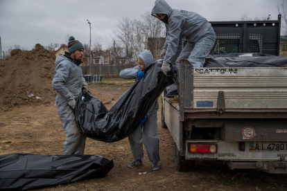 Autoridades forenses recogen cadáveres envueltos en plásticos para su traslado a la morgue, en Bucha.
