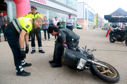 Un Mosso d'Esquadra ensenya a aixecar una moto de forma segura a un usuari de la jornada.