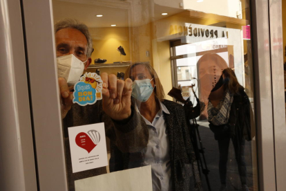 Un tendero de Valls, enganchando un adhesivo identificativo en la puerta de acceso.