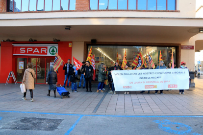 Dos mujeres entran en un supermercado Spar en Reus, mientras una veintena de trabajadores protestan.