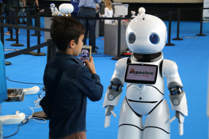 Un niño toma fotos y conversa con un robot humanoide.