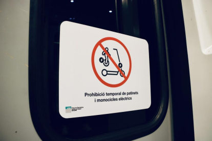 Cartell anunciant la prohibició temporal d'entrar amb patinets i motocicletes eléctriques al transport públic.