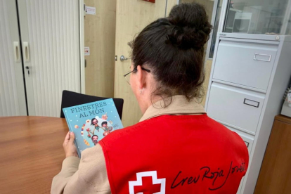 Una voluntària de Creu Roja d'esquenes subjectant un llibre.