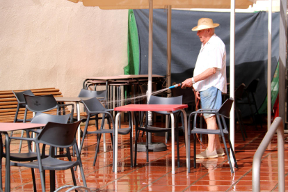 Un home refresca amb una mànega d'aigua la terrassa del local on els avis van a passar la tarda a Vinebre.