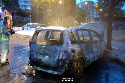 Un bombero rocía un turismo quemado en Reus.