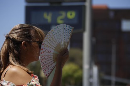 Una mujer se abanica junto a un termómetro de calle que marca 42 grados.