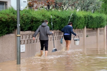 Un home i una dona caminant amb cubells per un dels carrers inundats de la urbanització La Móra de Tarragona.