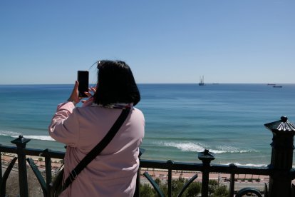 Una mujer fotografía el mar en Tarragona, ajena a la llegada de la plataforma de operaciones que sellará los pozos submarinos del proyecto Castor