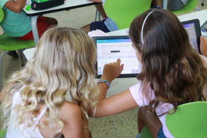 Dues nenes de Primària treballen amb una tauleta dins l'aula