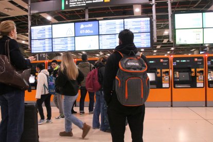 Persones mirant els panels informatius dels horaris de Rodalies a l'estació de Sants.