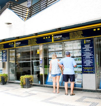 Una parella mira ofertes d'immobles penjades en una oficina de la immobiliària.