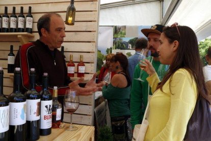 Una chica, con una copa en la mano, escuchando las explicaciones del responsable de una bodega de la Fira del Vi de Falset en su 24ª edición.