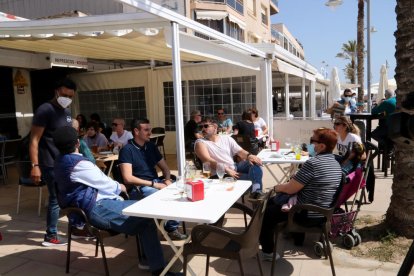 Pla general d'un grup de persones assegudes en una terrassa d'un bar del passeig marítim de Coma-ruga, al Vendrell, aquest Divendres Sant. Imatge del 2 d'abril del 2021