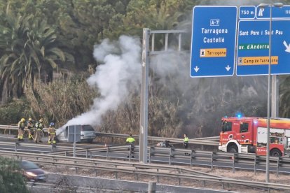 Los Bomberos trabajando con el vehículo incendiado.