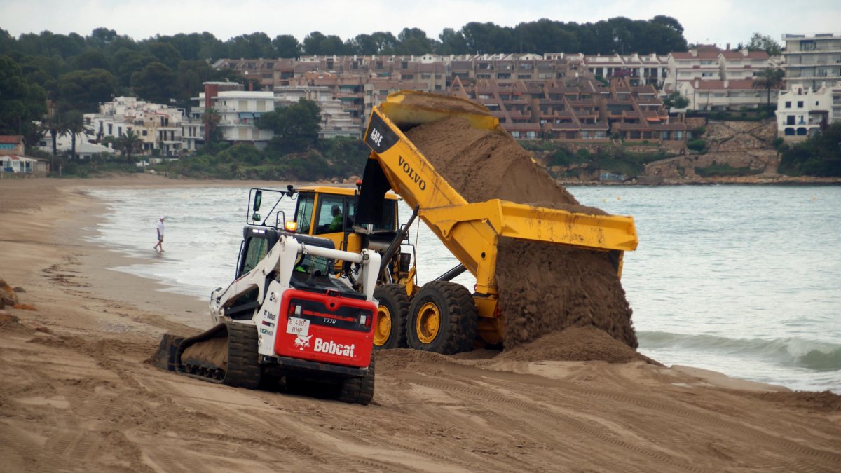 Un camió dipositant arena i una excavadora movent sorra a la platja d'Altafulla.