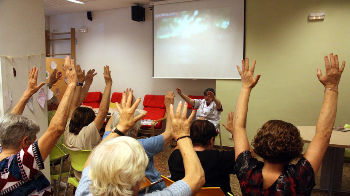 Un grupo de abuelos levantan las manos siguiendo las instrucciones de una terapeuta en un taller de psicomotricidad a la asociación AFAB para enfermos de Alzheimer.