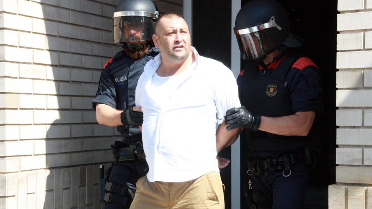 Uno de los detenidos escoltados por dos Mossos D'Esquadra en la salida de uno de los domicilios registrados del barrio del Templo de Tortosa.