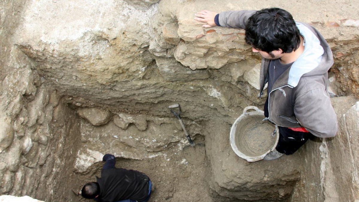 Un dels arqueòlegs treballant en l'excavació d'un sot al solar de la Catedral de Tortosa, amb l'ajuda d'un company des de la superfície.