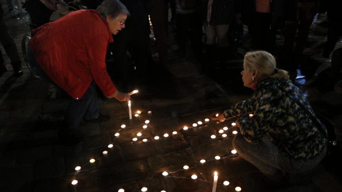 Plano cerrado de dos personas encendiendo velas para formar una silueta humana en la plaza del Mercadal.