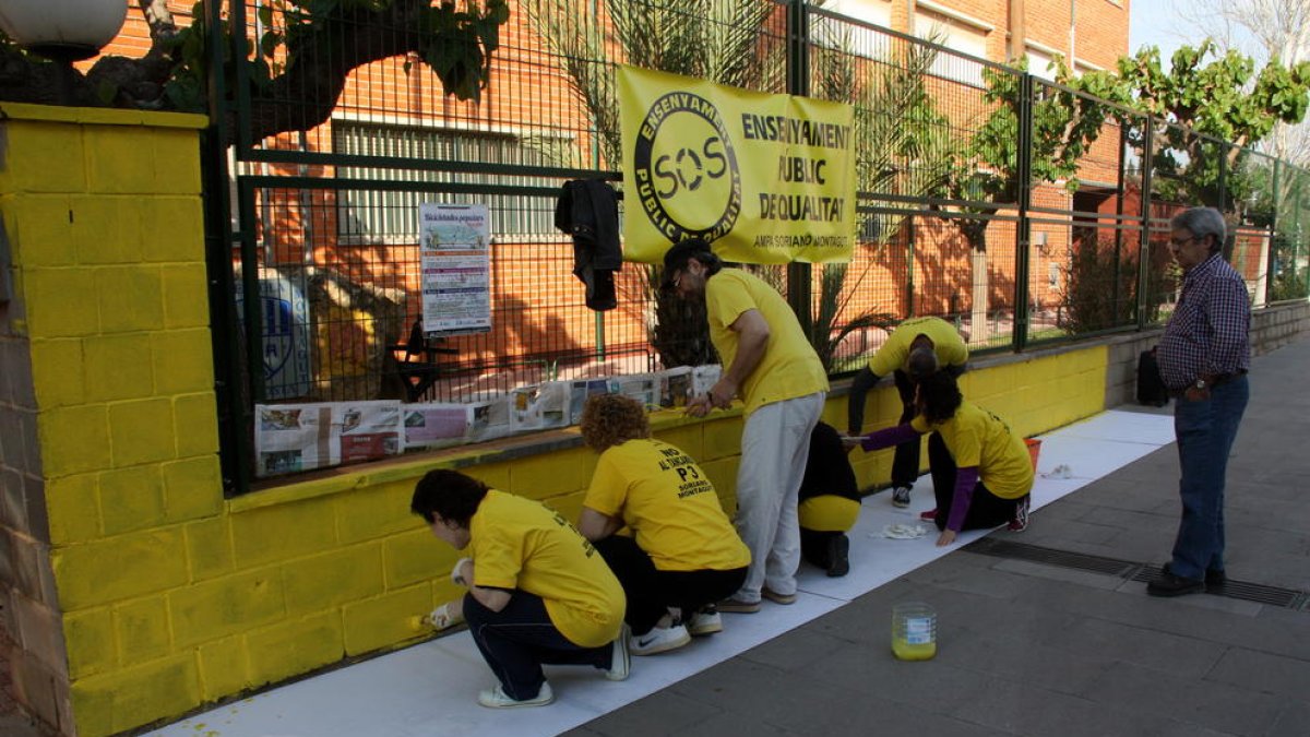 Un grup de mares i pares pintant el mur de l'escola Soriano Montagut d'Amposta. Imatge del 19 d'abril de 2016